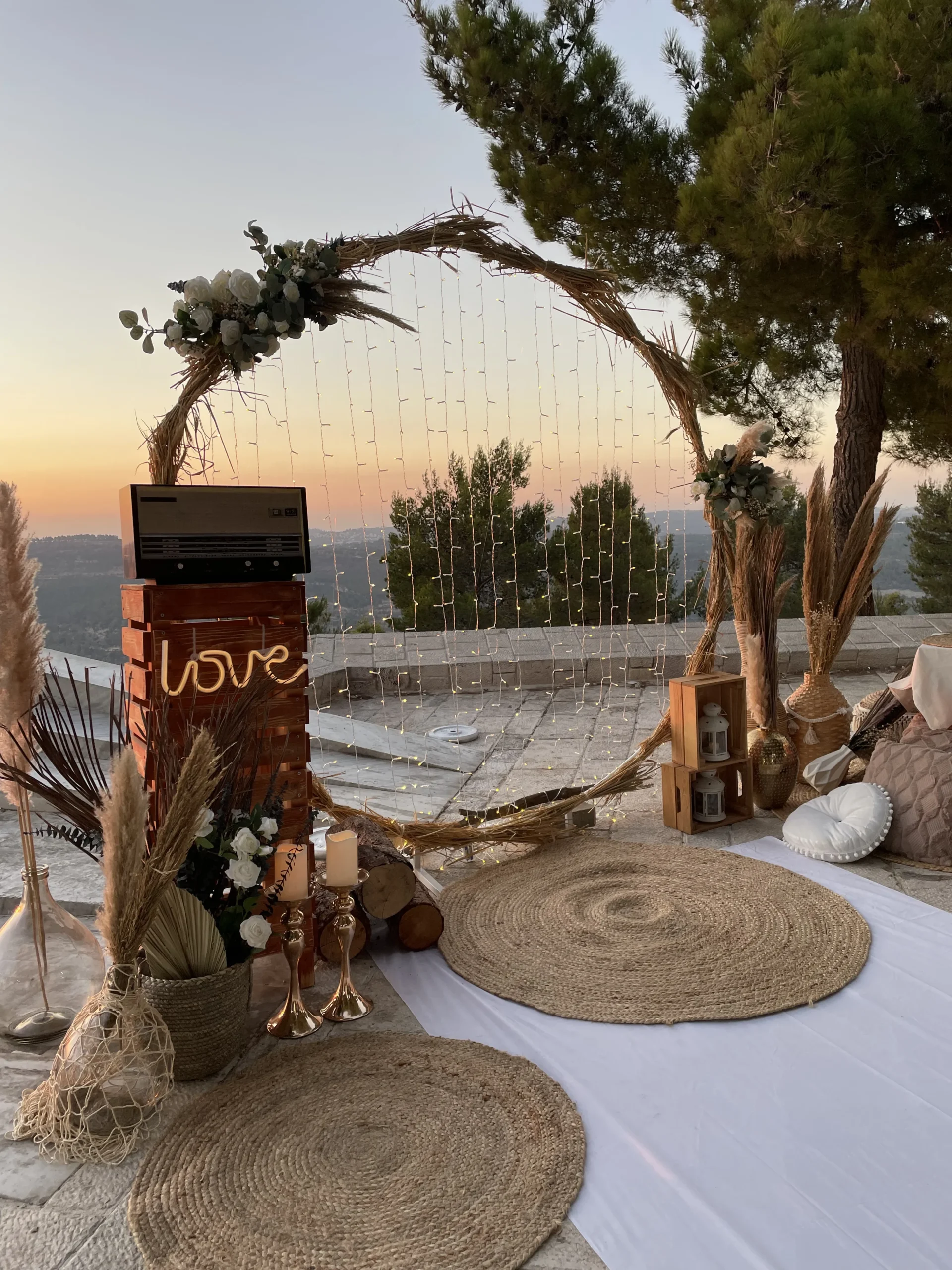 הצעת נישואין ייחודית בסגנון כפרי , המשלבת עמדת הצעה מעיגול קש ייחודי, תאורה עדינה ורכה ,זרי פרחים ייחודים, אביזרי נוי בסגנון בוהו ושביל בד תואם. הבחירה המושלמת להצעה אינטימית בנוף פסטורלי 3>