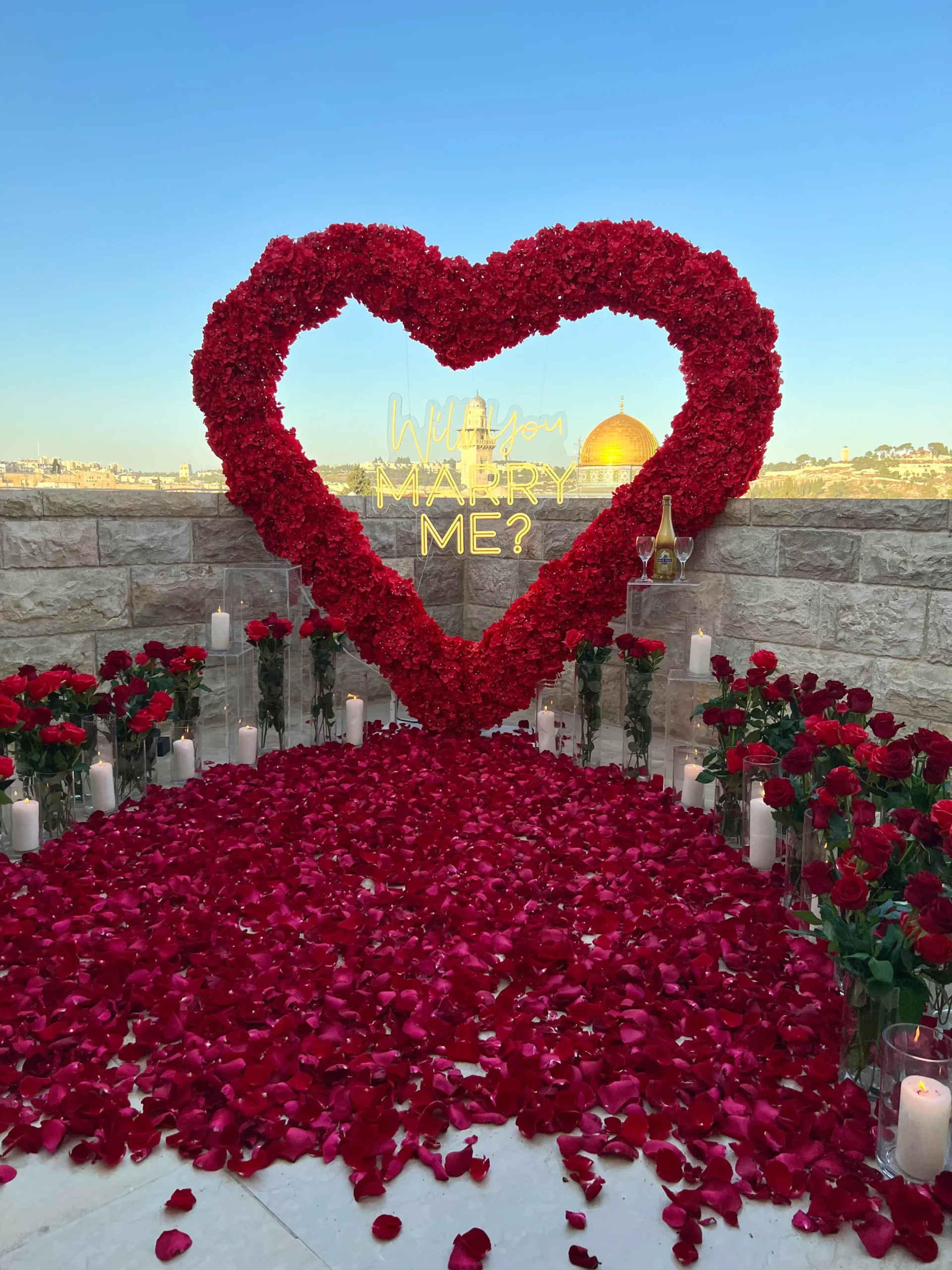 הצעת נישואין בעיצוב דרמטי ורומנטי במיוחד – לב ענק וייחודי מפרחים אדומים, סידור וורדים טריים כעלי כותרת, נרות בכל פינה וזרים עשירים משני צדי הלב. עיצוב שמדבר אהבה – באדום עוצמתי ובדיוק מושלם.