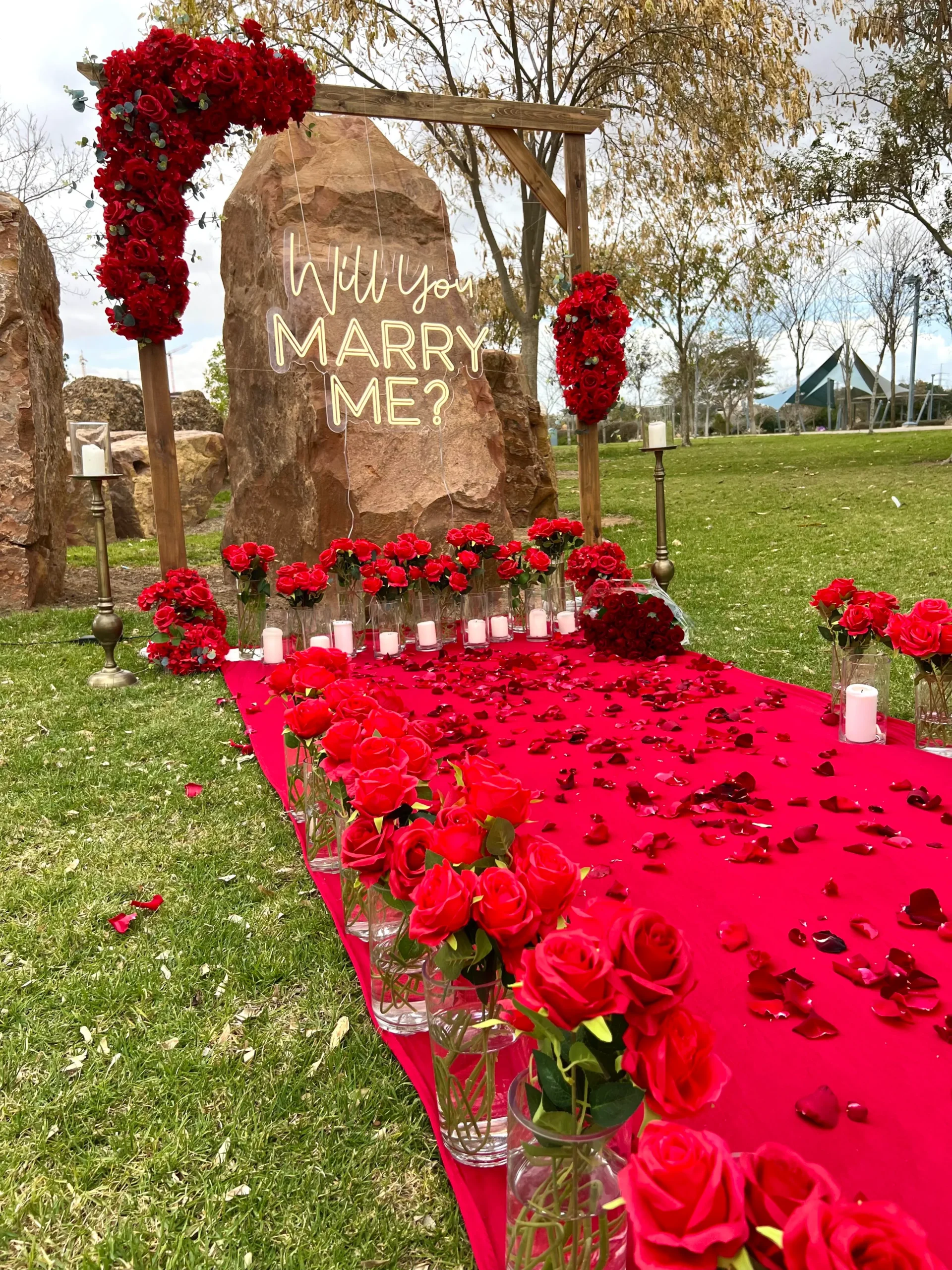 מעמד עץ ייחודי , מעוטר בזרי פרחים בגוון אדום בעיצוב סימטרי, מוקפד ומרשים - מוקף בנרות , זרי פרחים, שביל הליכה וסידור וורדים חיים כעלי כותרת ליצירת חוויה רומנטית ויוקרתית