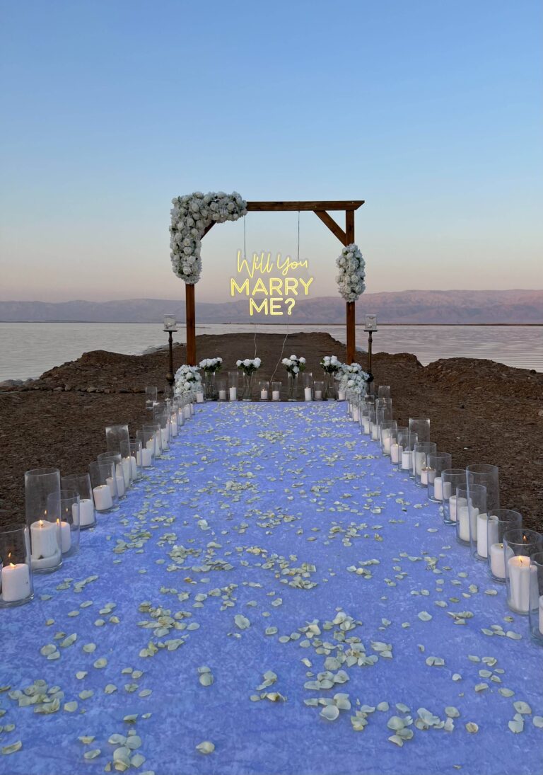 מעמד עץ ייחודי , מעוטר בזרי פרחים לבנים בעיצוב סימטרי, מוקפד ומרשים - מוקף בנרות , זרי פרחים, שביל הליכה וסידור וורדים חיים כעלי כותרת ליצירת חוויה רומנטית ויוקרתית