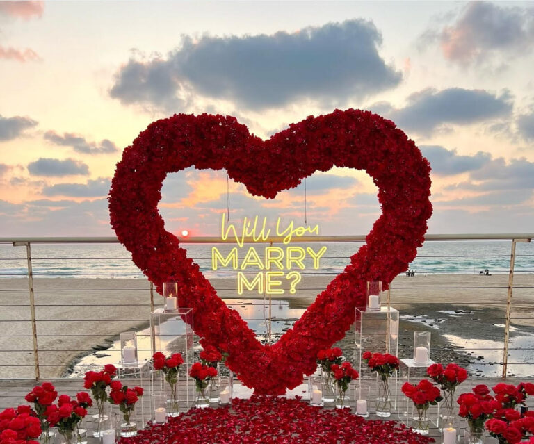 הצעת נישואין בעיצוב דרמטי ורומנטי במיוחד – לב ענק וייחודי מפרחים אדומים, סידור וורדים טריים כעלי כותרת, נרות בכל פינה וזרים עשירים משני צדי הלב. עיצוב שמדבר אהבה – באדום עוצמתי ובדיוק מושלם.