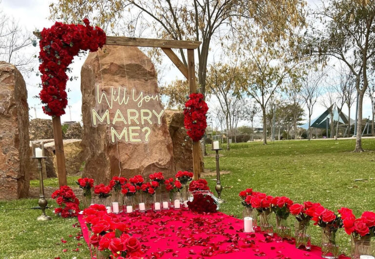 מעמד עץ ייחודי , מעוטר בזרי פרחים אדומים בעיצוב סימטרי, מוקפד ומרשים - מוקף בנרות , זרי פרחים, שביל הליכה וסידור וורדים חיים כעלי כותרת ליצירת חוויה רומנטית ויוקרתית