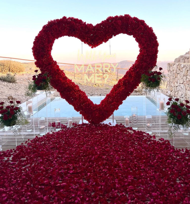 הצעת נישואין בעיצוב דרמטי ורומנטי במיוחד – לב ענק וייחודי מפרחים אדומים, סידור וורדים טריים כעלי כותרת, ריבוי וואזות ונרות , ושזירת ארבעה זרי פרחים חיים משני צדי הלב. עיצוב שמדבר אהבה – באדום עוצמתי ובדיוק מושלם.