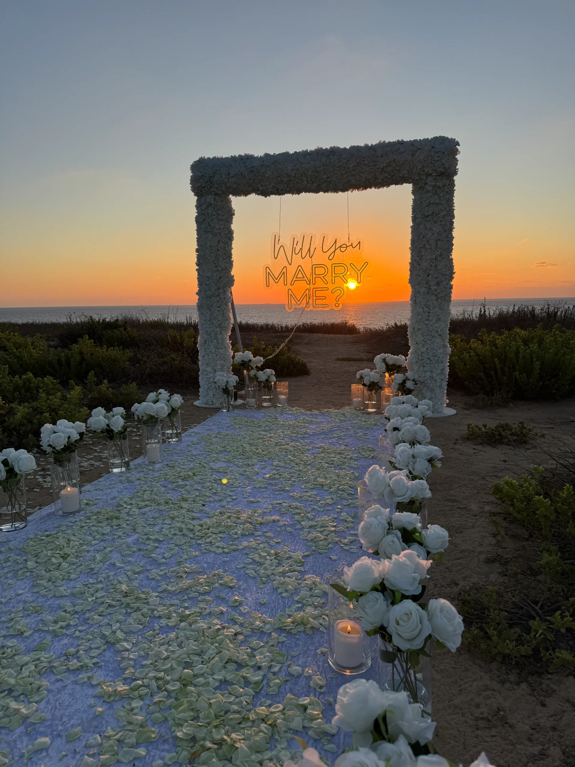 מעמד פרחים לבן ועוצמתי בעיצוב סימטרי, מוקפד ומרשים - מוקף בנרות , זרי פרחים, שביל הליכה קסום מעוטר בעלי כותרת מוורדים היוצרים ליצירת אווירה רומנטית ויוקרתית